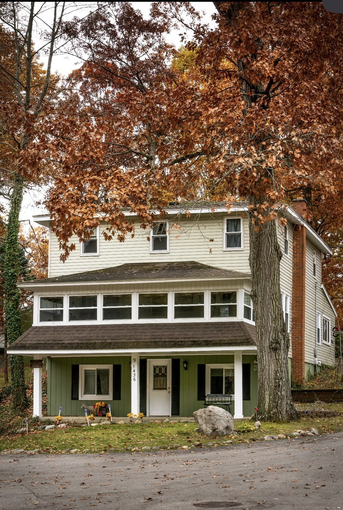 Three-story lake house with a long enclosed sunporch, green porch and an oak in autumn color
