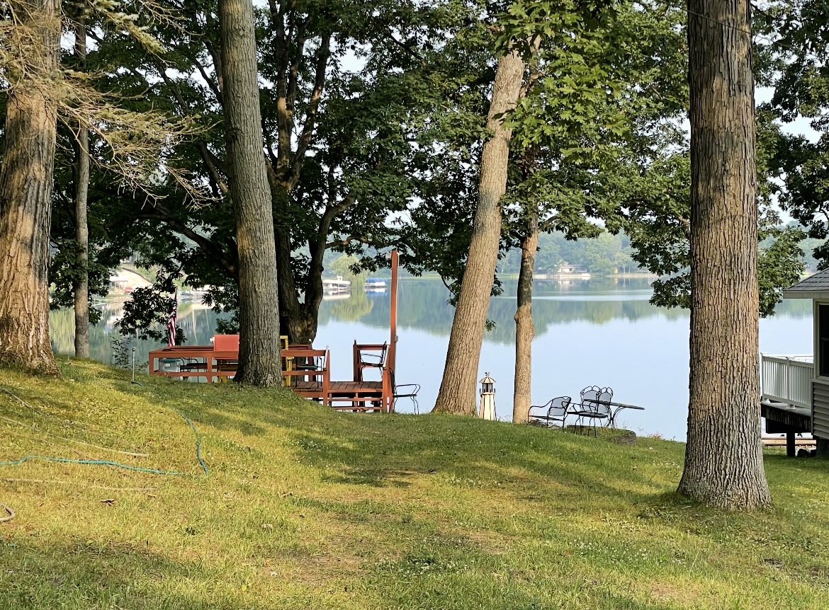 Shaded lawn sloping down through mature trees to a deck and the lake beyond
