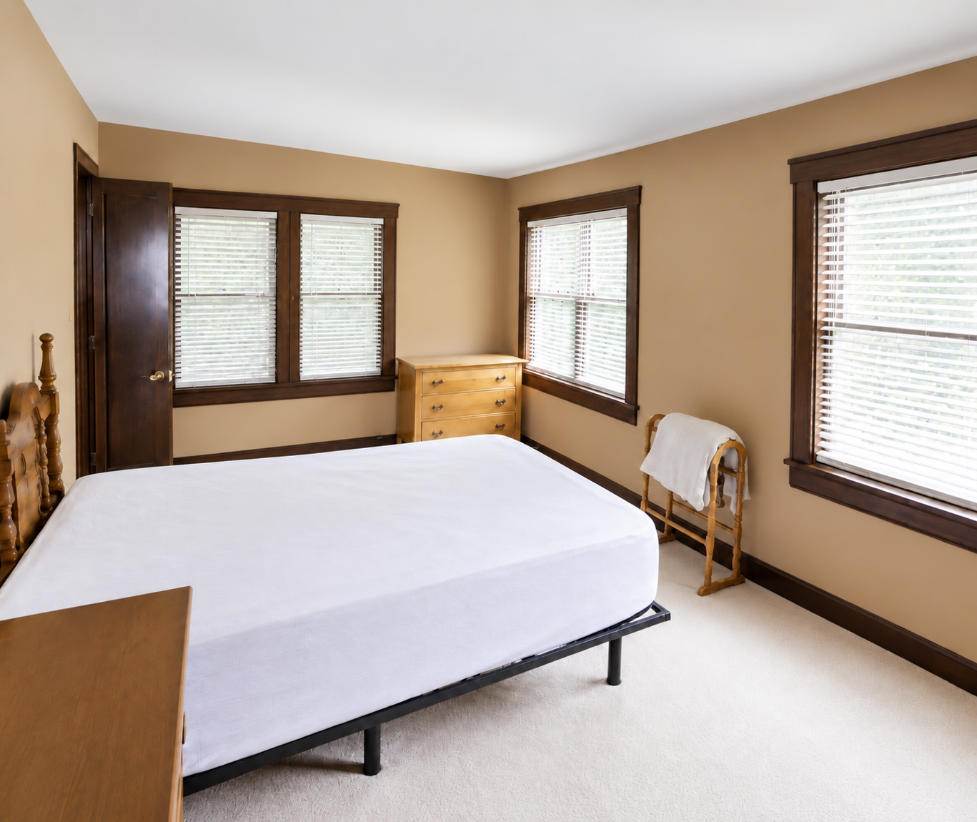Bedroom with tan walls, dark wood trim, three sunlit windows and a wooden bed