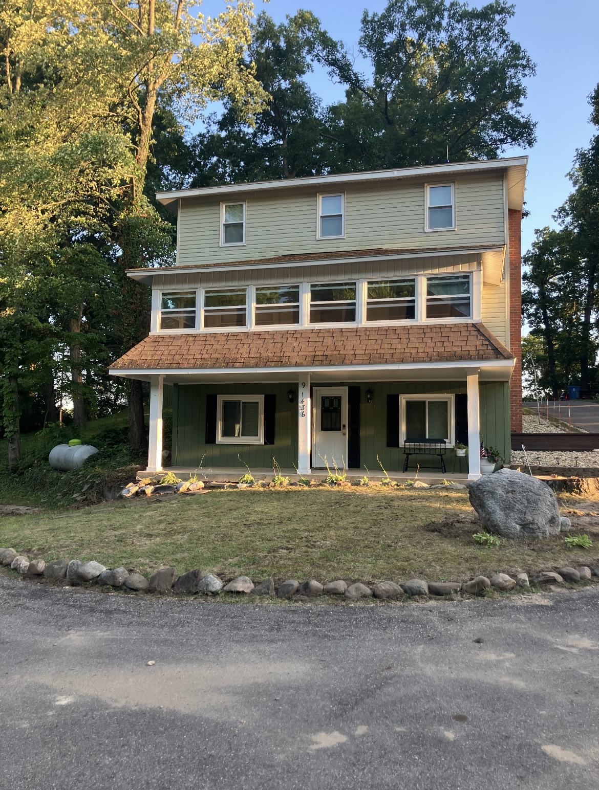 Green three-story lake house at 91436 with a covered front porch and a long band of sunporch windows above