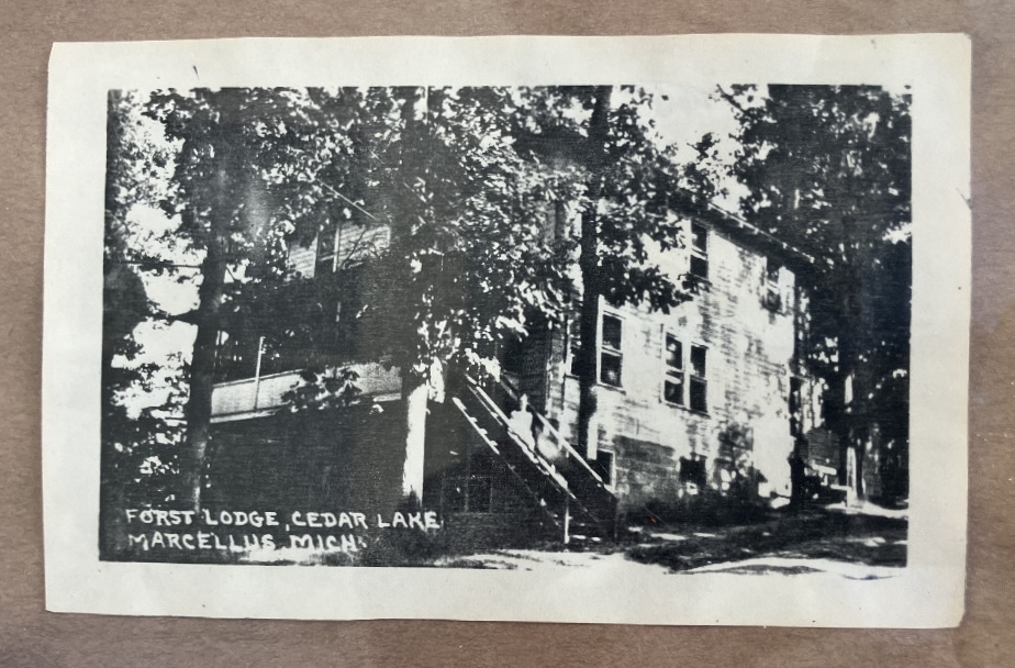 Matted black and white postcard of a three-story lodge under heavy trees, hand-lettered Forst Lodge, Cedar Lake, Marcellus Mich.