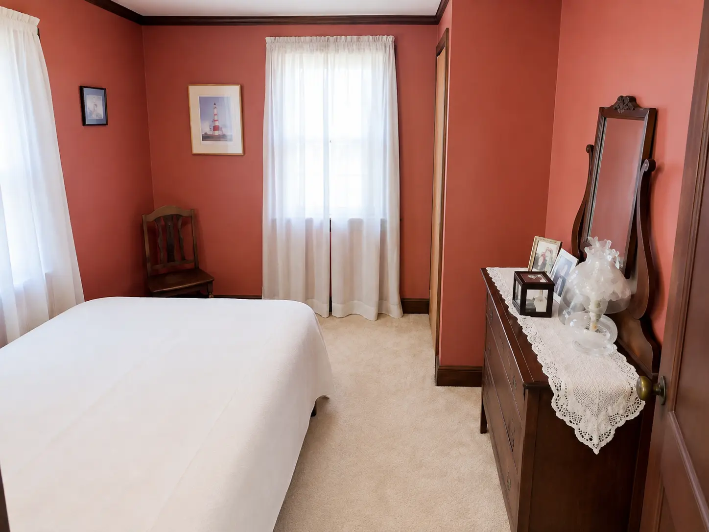 Bedroom with terracotta walls, white curtains and an antique mirrored dresser