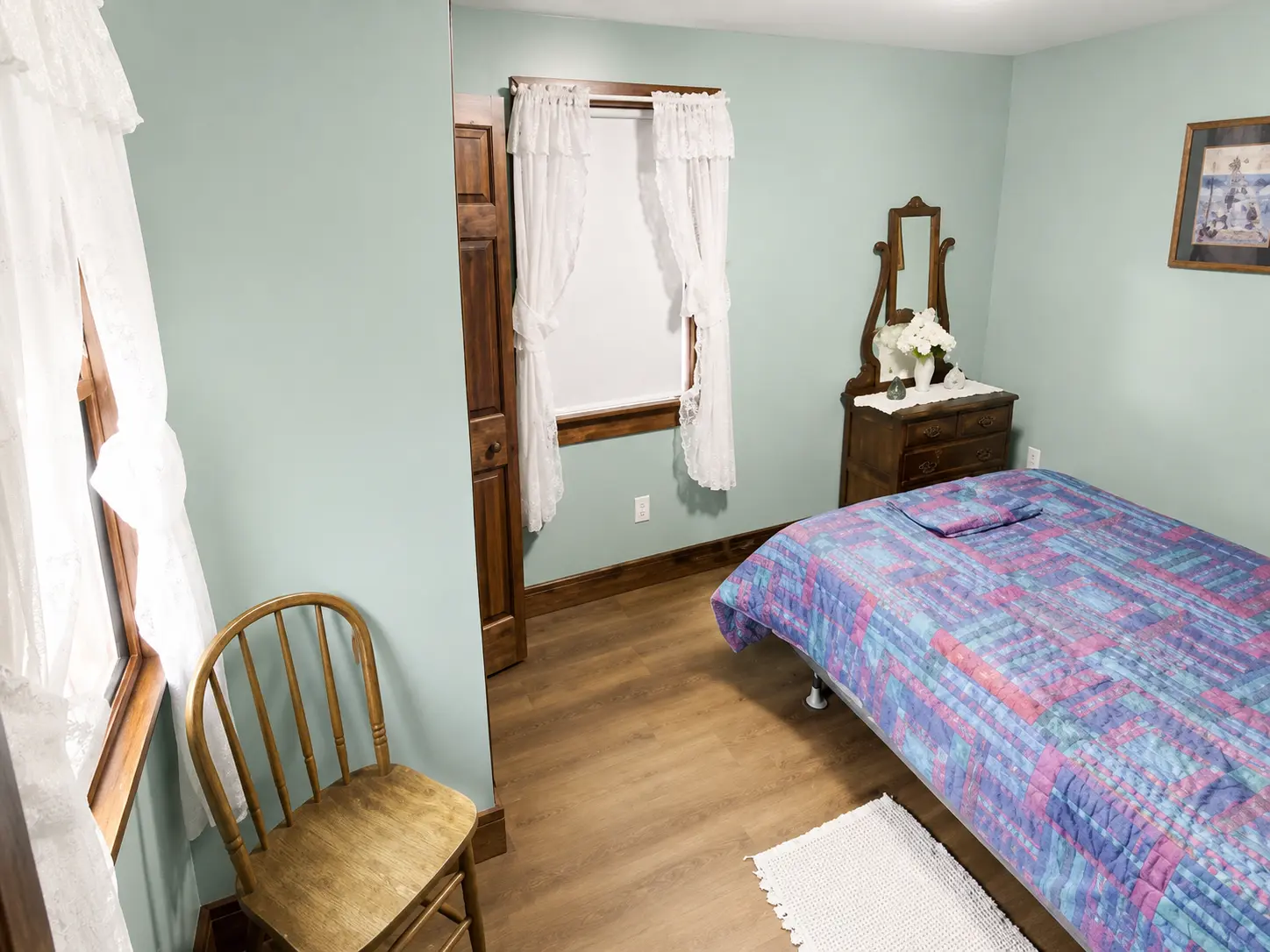 Bedroom with sage green walls, lace curtains and a patchwork quilt on the bed